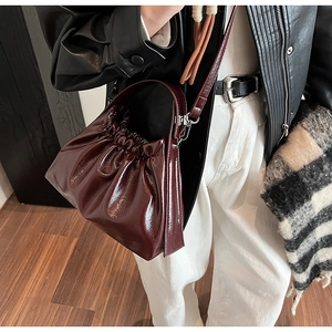 Detail of a dark red glossy pleated cloud bag with leather texture and silver buckle