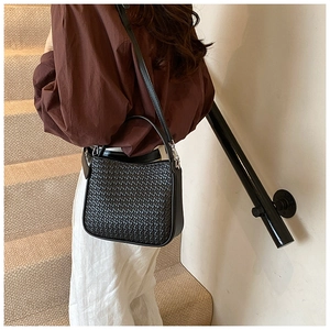 Rear view of model wearing a black woven PU leather crossbody bag with top handle and strap