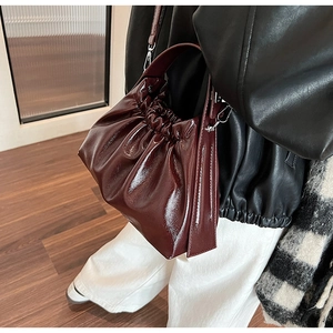 Detail of burgundy ruched cloud bag showing glossy leather texture and thin strap