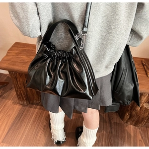 Detail of glossy black pleated cloud bag with detachable strap shown on a wooden bench