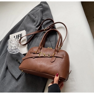 Detail of brown lychee texture leather handbag with golden hardware on grey blazer
