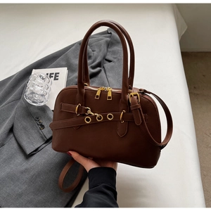 Close-up of brown leather bag featuring golden zipper and decorative ring hardware