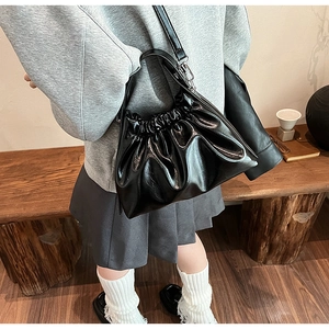 Detail of black pleated cloud bag on wooden bench showing soft leather texture and strap