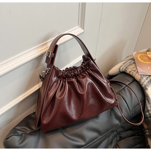Detail view of burgundy pleated dumpling bag with glossy leather texture and silver hardware