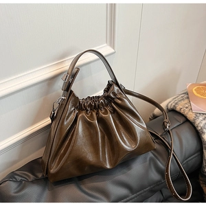 Detailed view of dark coffee pleated cloud bag with soft PU leather on a black leather sofa