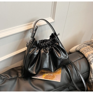 Detail of black pleated cloud bag with glossy patent leather texture and silver hardware