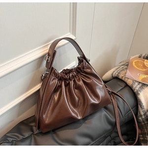 Close-up of dark brown ruched cloud bag with glossy faux leather texture on black bench