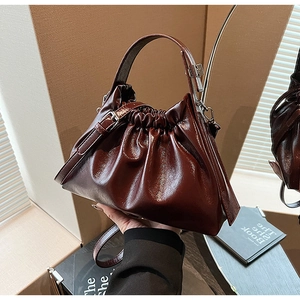 Detail of a dark brown ruched cloud bag with glossy leather texture and stylish chain