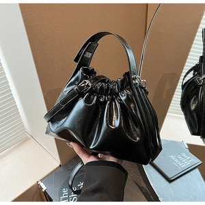 Detailed close-up of glossy black ruched dumpling bag with adjustable strap and handle