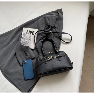 Detail view of a black tote bag with gold hardware and studs on a styled white surface