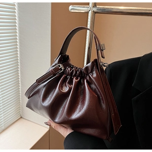 Detail showing the glossy dark burgundy pleated cloud bag with silver ring handle accents