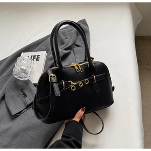 Detail of black leather handbag with gold hardware zippers on a grey blazer background