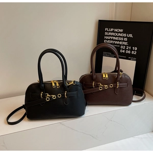 Detail view of black and coffee leather Boston bags with gold hardware on marble