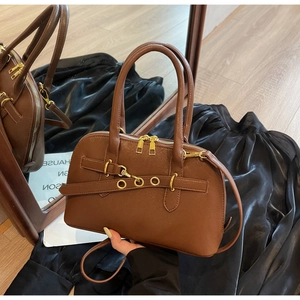 Detail of a brown leather handbag featuring golden metal rings and dual zipper closure