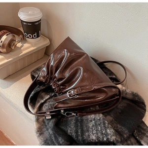 Detail of dark brown ruched dumpling bag with glossy finish on a plaid blanket