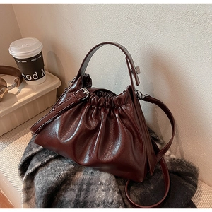 Detail of burgundy ruched cloud bag showing metallic buckle strap and glossy texture