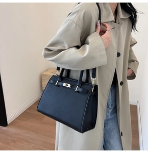 Dettaglio della borsa in pelle nera con fibbia dorata su modella con trench beige