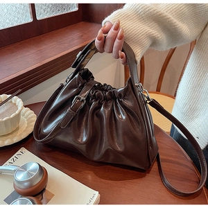 Detail of dark brown ruched cloud bag on a wooden table with a vintage coffee vibe