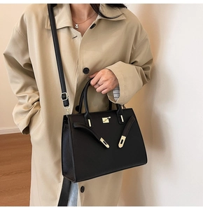 Dettaglio borsa a mano in pelle nera con fibbie dorate e doppi manici sopra il cappotto