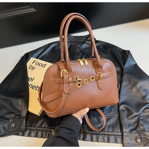 Detail of a brown leather bowling handbag with gold hardware and dual handles