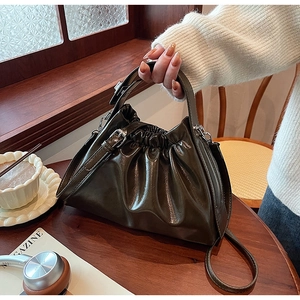 Detail of olive green ruched dumpling bag on a wooden table with lifestyle props