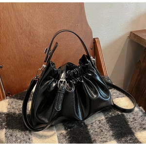 Detail of glossy black pleated cloud bag with silver hardware on checkered blanket
