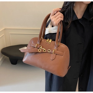 Detail of a brown leather handbag featuring golden metal rings and dual zipper closure