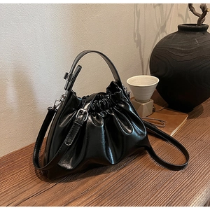 Macro detail of glossy black cloud bag featuring pleated design and silver metal hardware