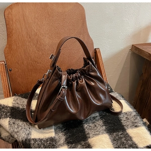Detailed view of a dark brown ruched cloud bag on a vintage wooden chair with texture