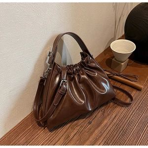 Detailed view of the dark brown pleated handbag with a glossy oil-wax finish and silver hardware