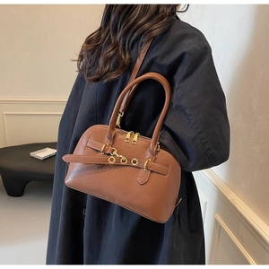 Detail of a brown leather bowling bag with gold hardware and cylindrical handles