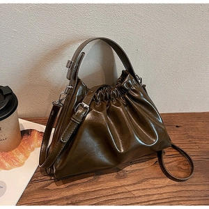 Detail of olive green ruched cloud bag in glossy finish on a rustic wooden table