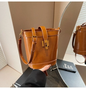 Détail d'un sac seau en cuir marron avec fermoir tournant doré et bandoulière réglable