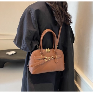 Brown vintage top-handle bag worn cross-body by a model in a minimalist room