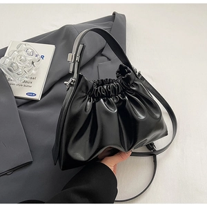 Detail of black glossy pleated handbag featuring silver hardware and drawstring closure