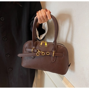 Close-up of brown Boston handbag featuring decorative thin straps and gold metal buckles