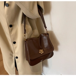 Brown vintage flap bag featuring a gold flower clasp worn with a beige trench coat