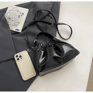 Detail of black glossy ruched cloud bag with adjustable strap on grey blazer fabric