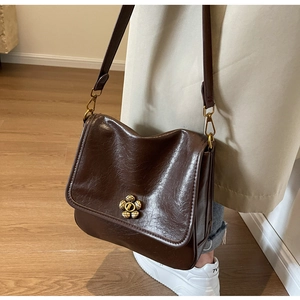 Detail of vintage brown crossbody bag with gold flower clasp worn with a beige trench coat