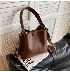 Detail of brown leather bucket bag with wide strap on a minimal white prop book