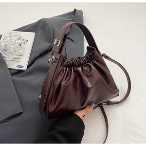 Detail of burgundy ruched cloud bag showing glossy texture on a grey blazer