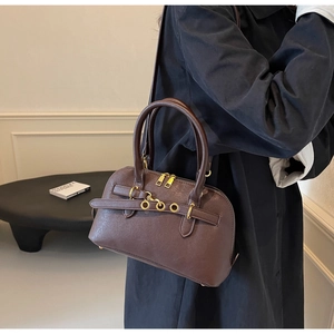 Detail of dark brown leather crossbody bag with gold zippers and decorative metal eyelets