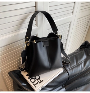 Close-up of black leather bucket bag featuring a wide strap and striped woven shoulder strap