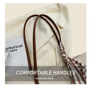 Detail of beige tote bag featuring a brown strap wrapped in a stylish plaid scarf