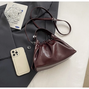Close-up of burgundy glossy pleated cloud bag with adjustable strap and smartphone scale
