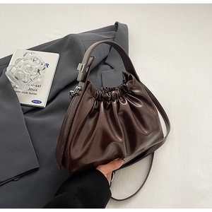 Detail view of a dark brown pleated cloud bag on a gray blazer highlighting glossy PU leather