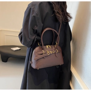 Detail of dark brown matte leather handbag with decorative metal eyelet and dual handles