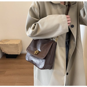 Detail of dark brown vintage crossbody bag featuring a golden flower clasp on beige coat