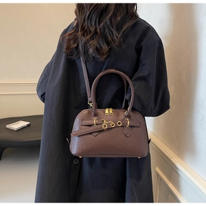 Detail of a dark brown crossbody bag with gold buckle on an elegant leather surface