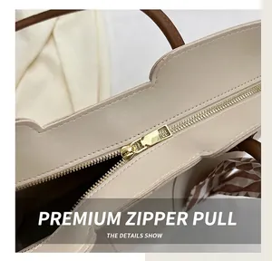 Close-up of golden metal zipper detail and brown plaid scarf on a beige tote bag